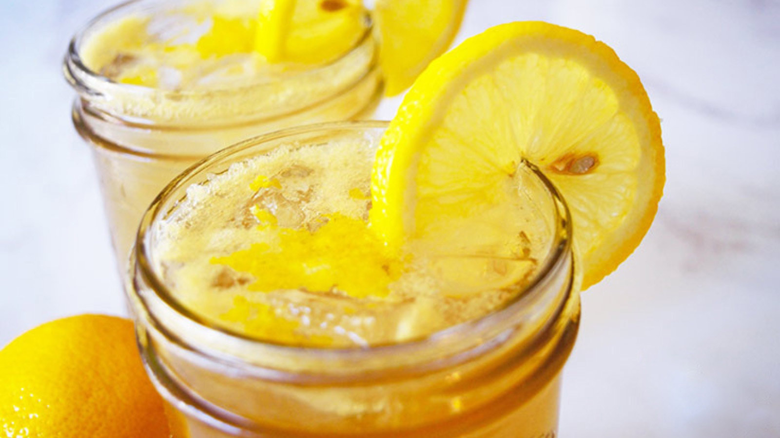 An up close view of the tops of two glass jars, filled with Lemon Drop Mocktail and garnished with lemon slices.
