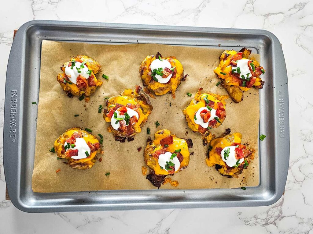Loaded smashed potatoes on a sheet pan sprinkled with chopped green onions.