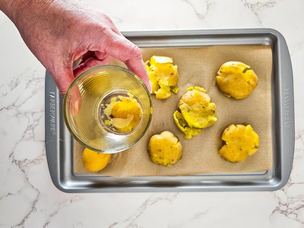 Smashing small potatoes on a baking sheet with a glass.