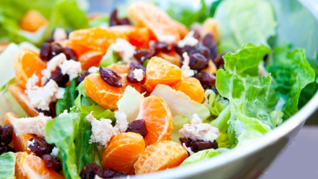 A metal bowl filled with Mandarin Orange Chicken Salad With Dried Cranberries.