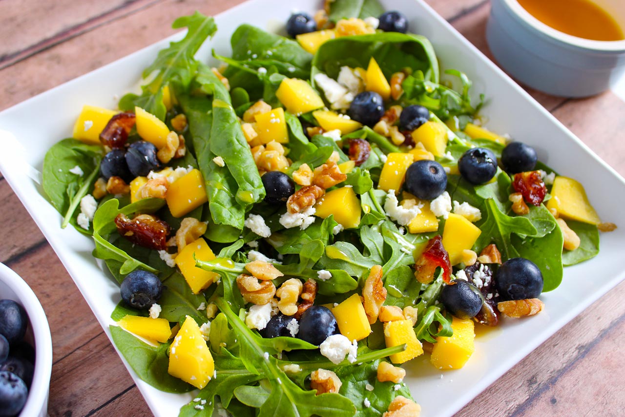 A white platter on a wood surface, holds a Mango Blueberry Salad.