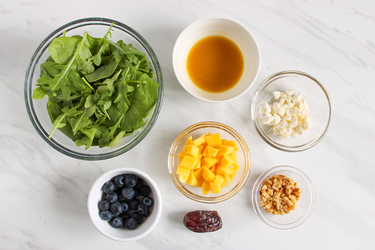 Ingredients for this Mango Blueberry Salad Recipe in individual bowl on a white marble surface.