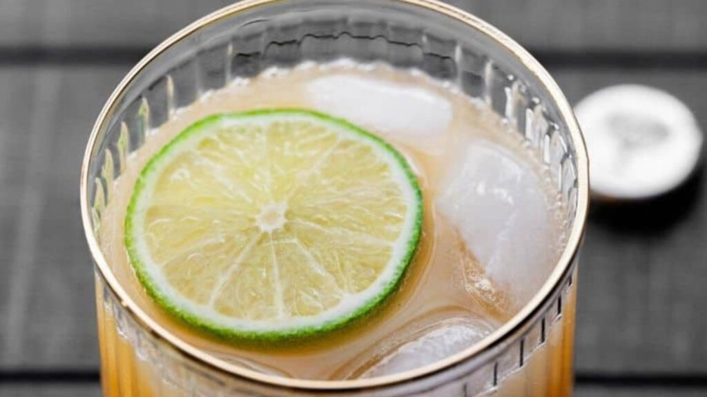 A closeup of a glass of mango mocktail with a lime slice and ice in it.