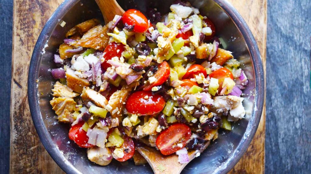 An overhead view of a mixing bowl with tongs in it, filled with The Best Greek Chicken Salad.
