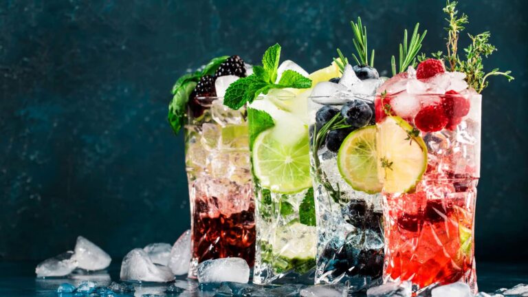 Mocktails drinks. Classic long drink or mocktail highballs with berries, lime, herbs and ice on blue background