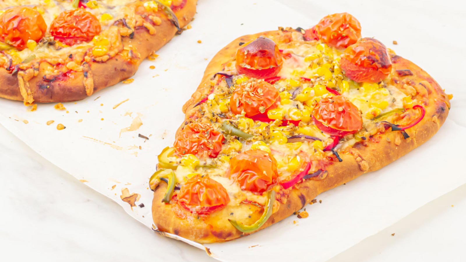 Two naan pizzas on white parchment.
