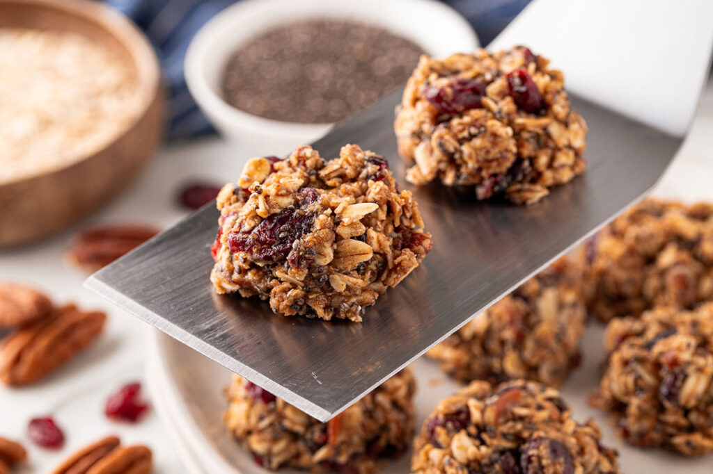 A spatula lifts 2 no-bake cookies up off of a cookie sheet.