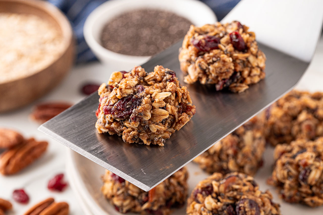 A spatula lifts 2 no-bake cookies up off of a cookie sheet.