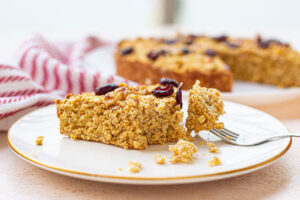 A fork holds a bit of Oatmeal Cake from a slice on the plate it is laying on.