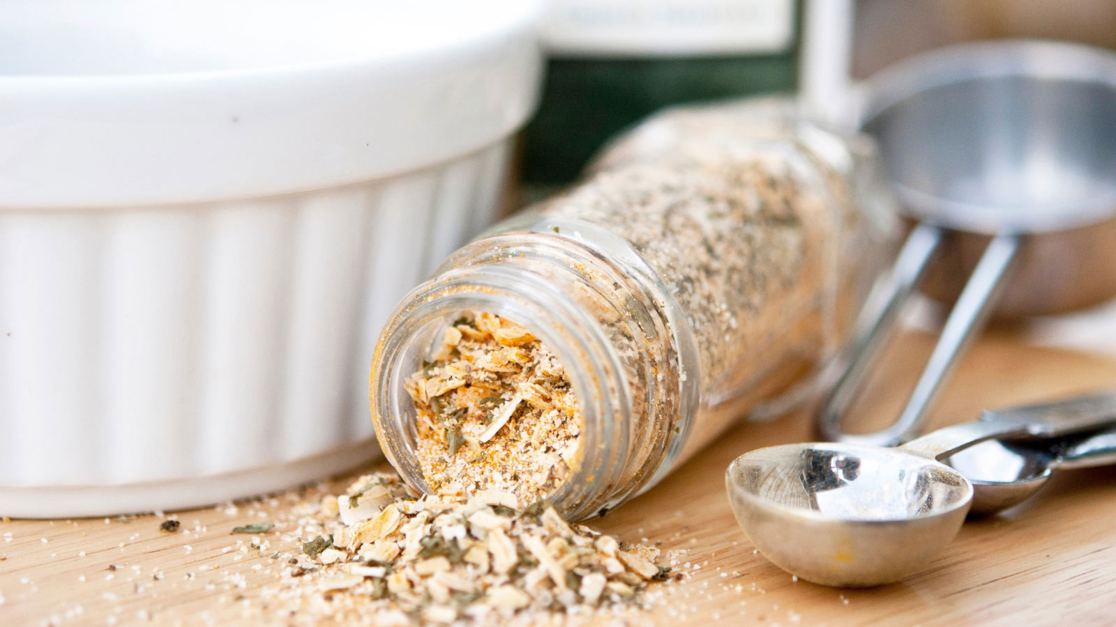 A tipped-over, open jar of onion soup mix on a wood cutting board.