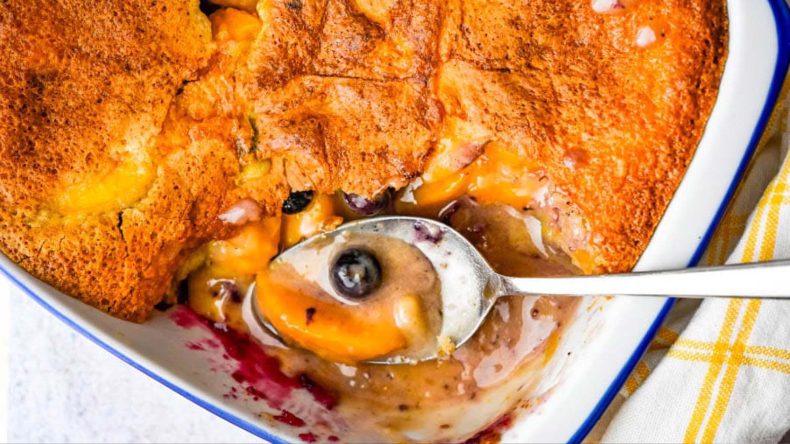 An overhead view of a partially eaten peach blueberry cobbler in a casserole dish.