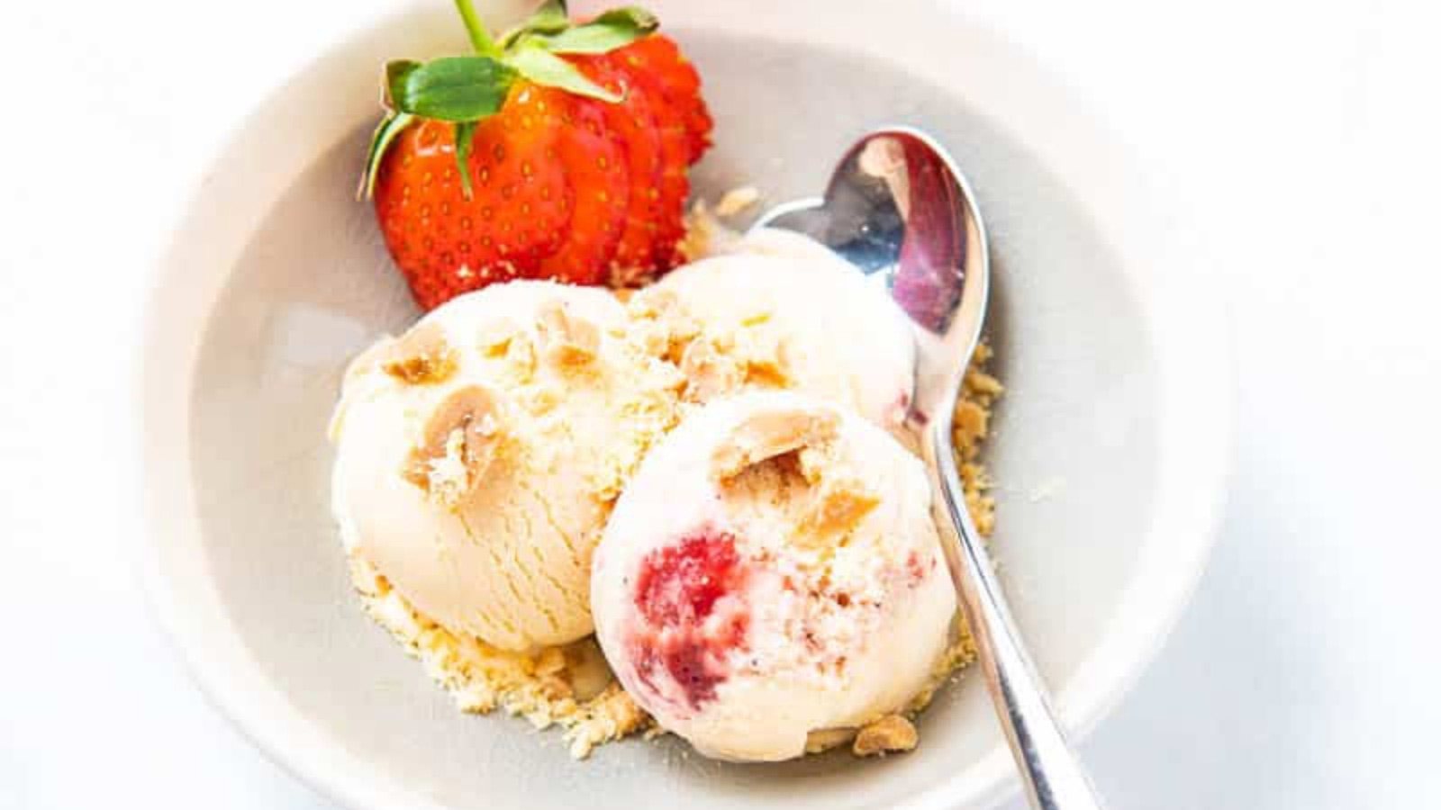 A white bowl with three scoops of peanut butter and jelly ice cream and a spoon in it.