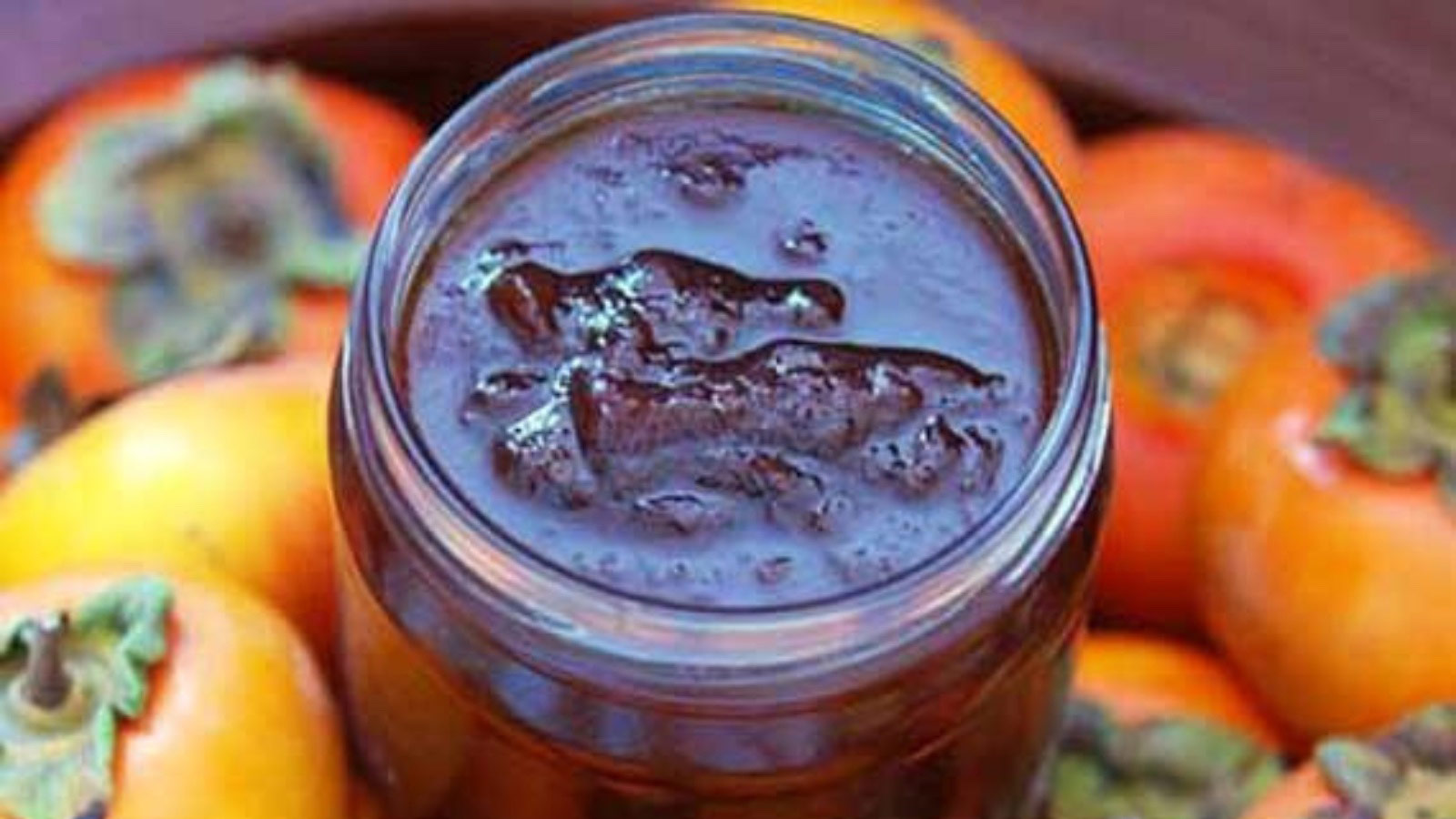 Persimmon Jam in an open jar, surrounded by persimmons.