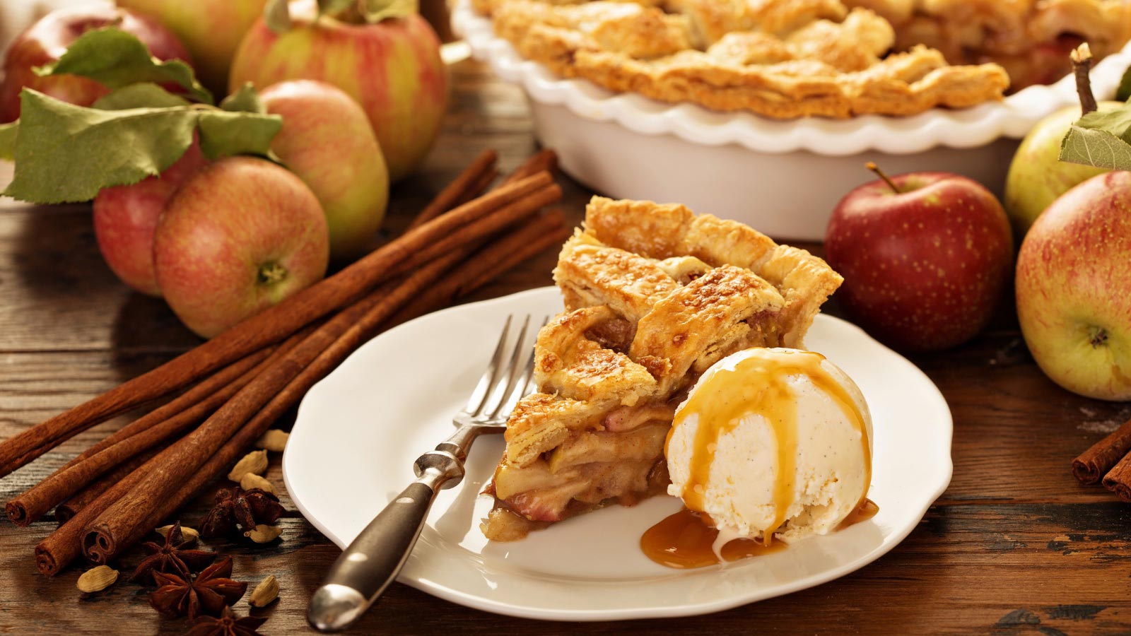 Piece of an apple pie with ice cream scoop and caramel sauce on a plate.