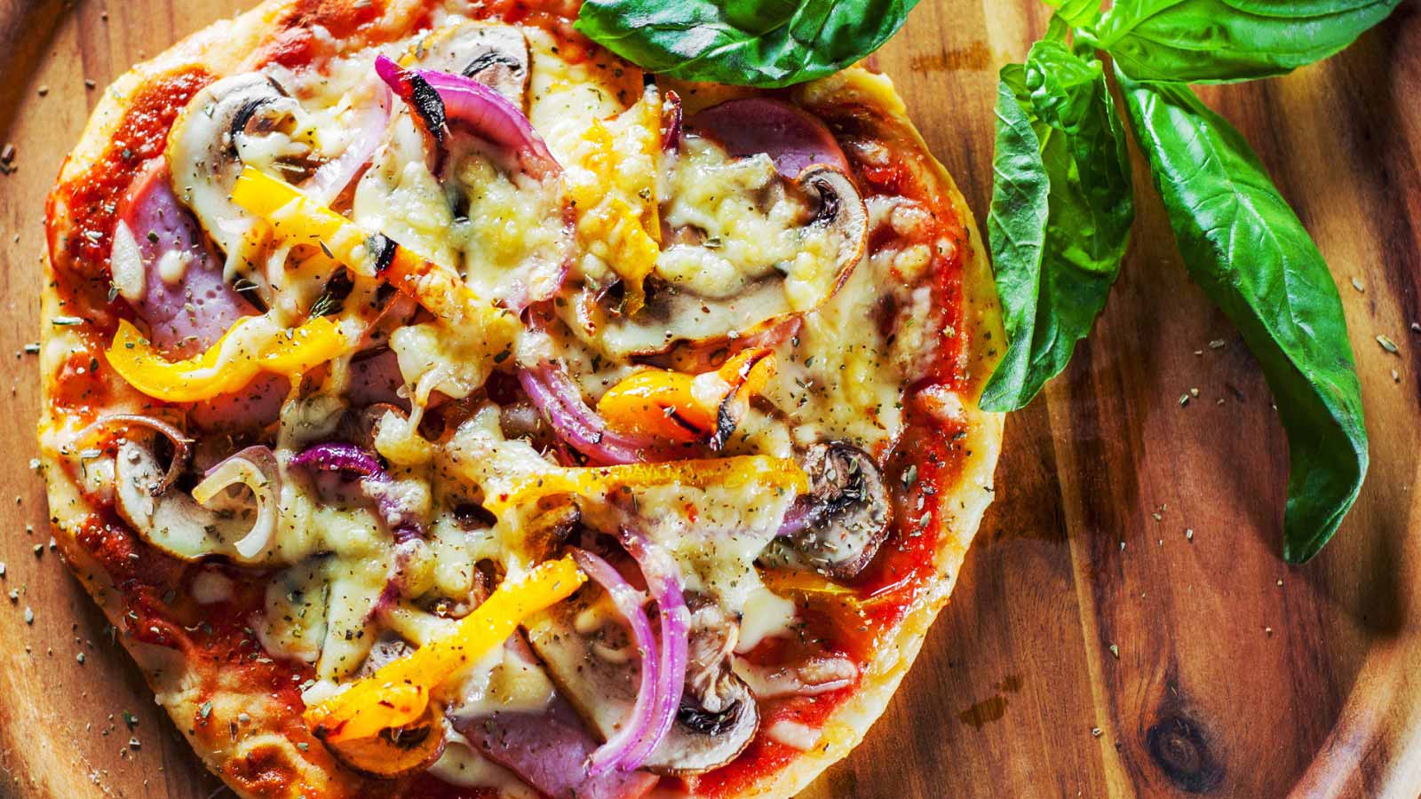 Greek pizza with mushrooms, ham, cheese, onions, pepper on wooden board.