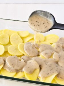 Adding white sauce to the first layer of potatoes in a casserole dish.