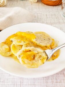 A fork lifts some potatoes au gratin from a white plate.