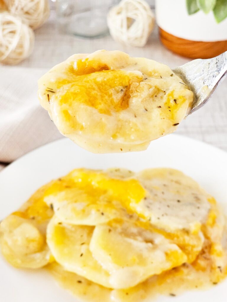 A serving spoon lifts up a spoonful of potatoes au gratin from a dish.