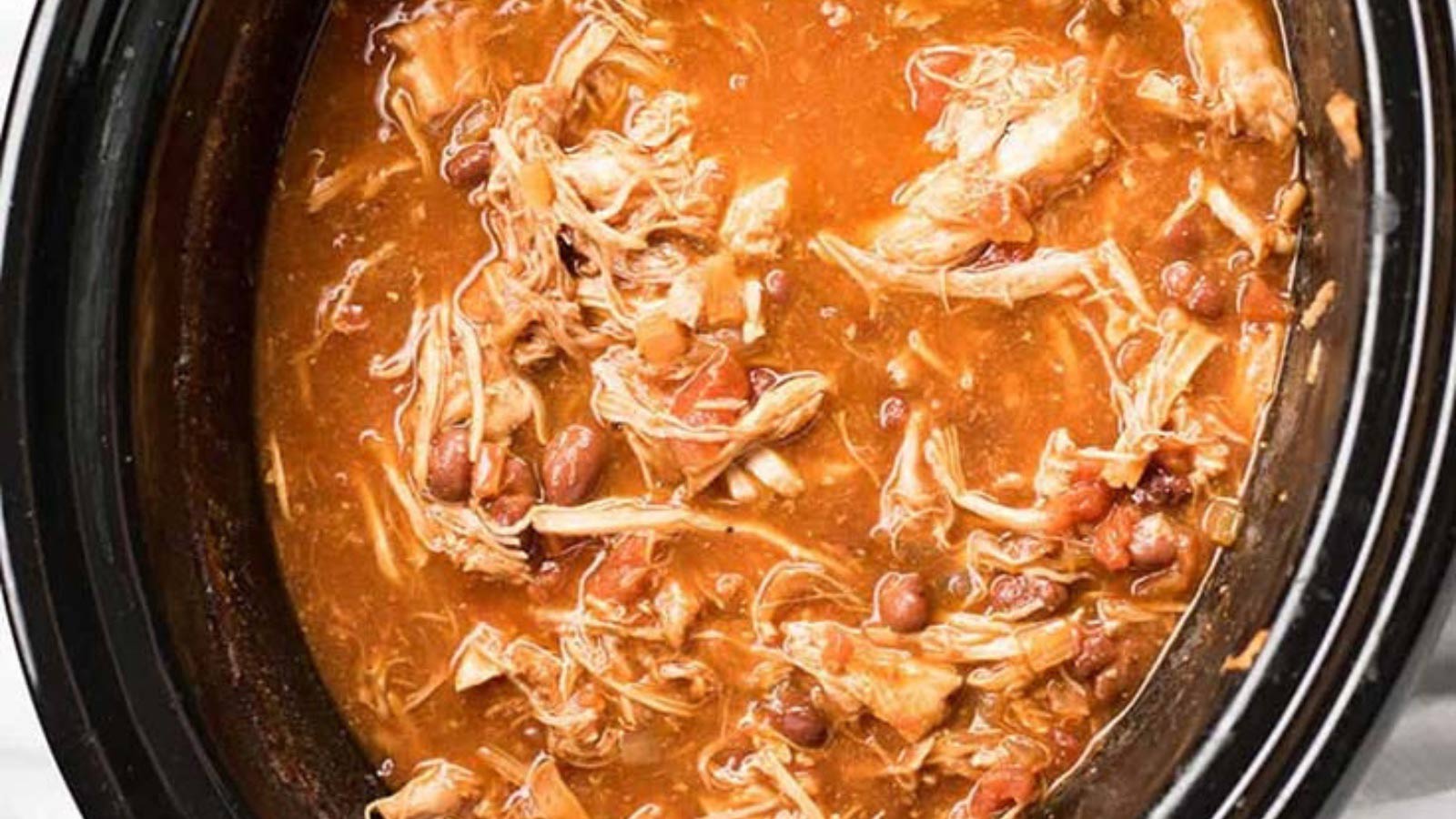 An overhead view of pulled pork chili in a black slow cooker crock.