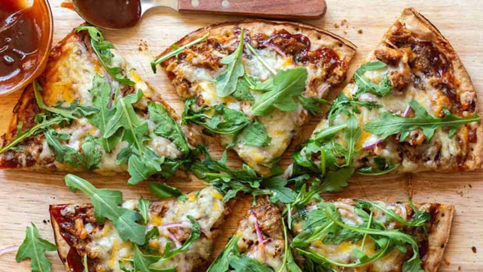 An overhead view of a cut, pulled pork pizza on a cutting board.