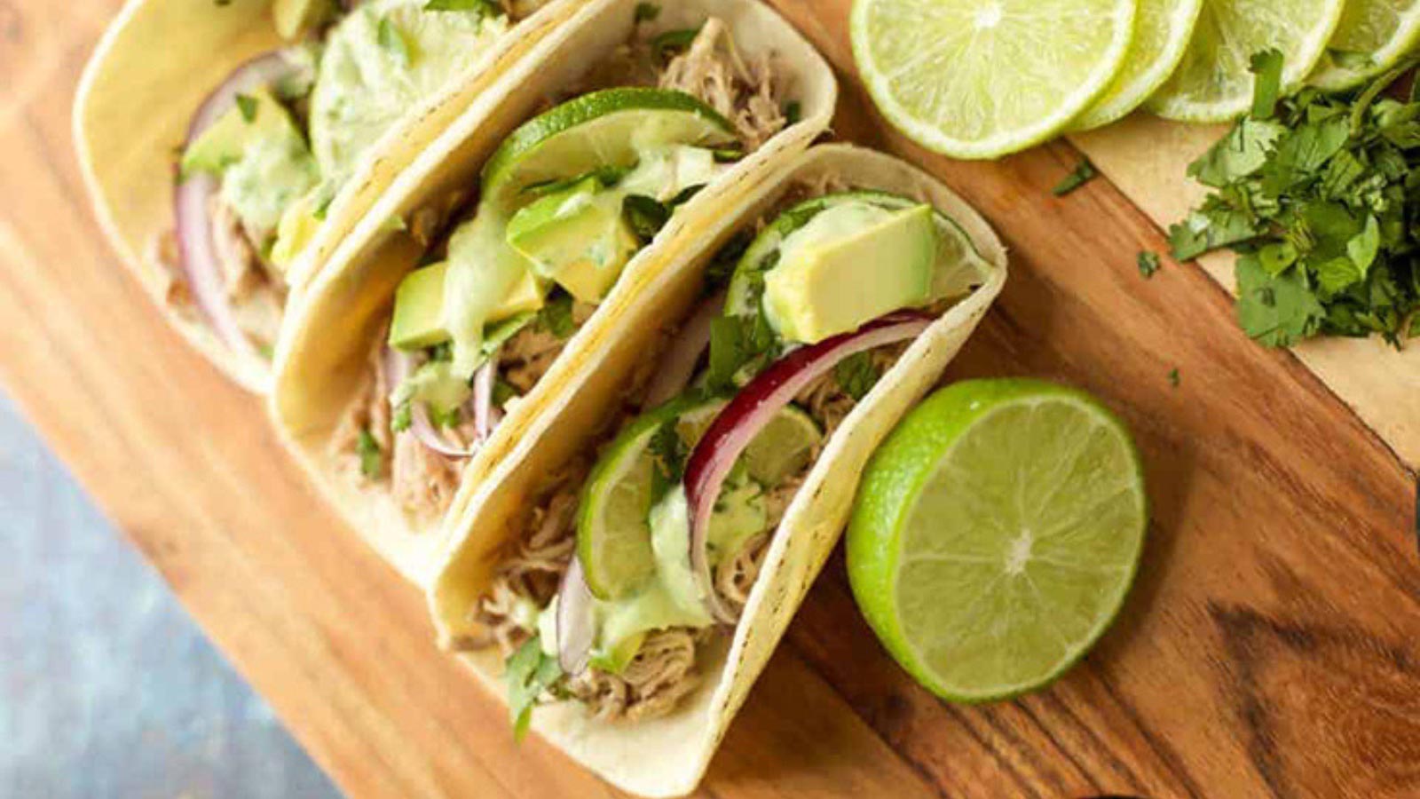 A cutting board with three pulled pork taos and some lime slices on it.