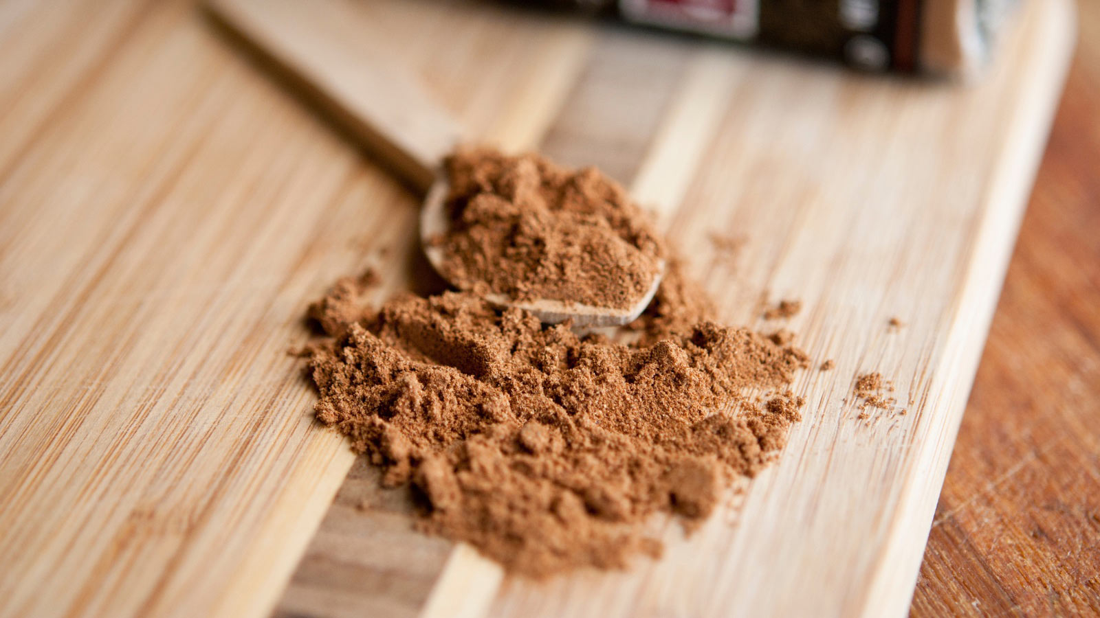 A wooden spoon filled with pumpkin pie spice laying on a cutting board.