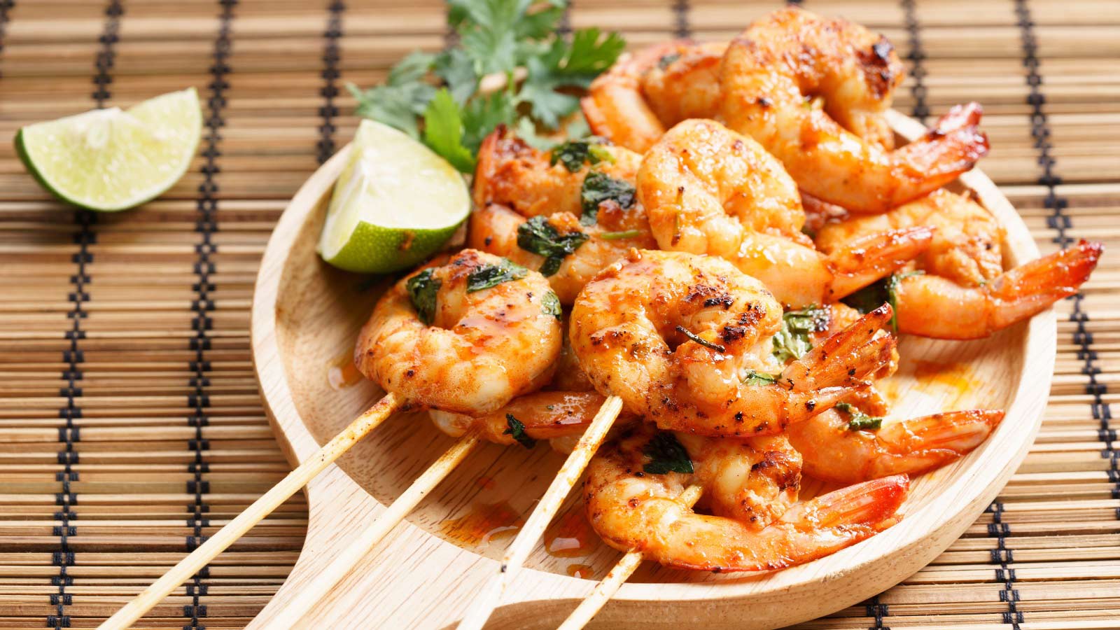Shrimp kebabs with lime and cilantro leaves on a wood platter.