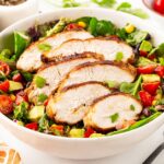 A white bowl of Southwest Salad topped with slices of chicken breast.
