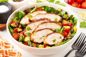 A white bowl of Southwest Salad topped with slices of chicken breast.