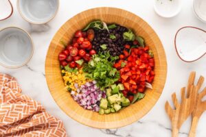 Southwest Salad ingredients added to lettuce in a wooden serving bowl.
