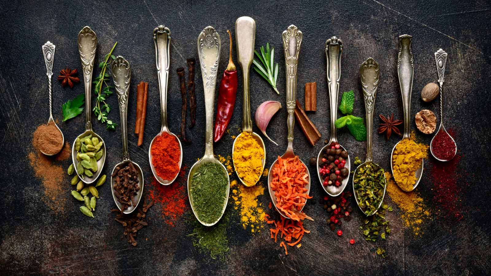 Assortment of natural spices on a vintage spoons over dark slate, stone, concrete or metal background.