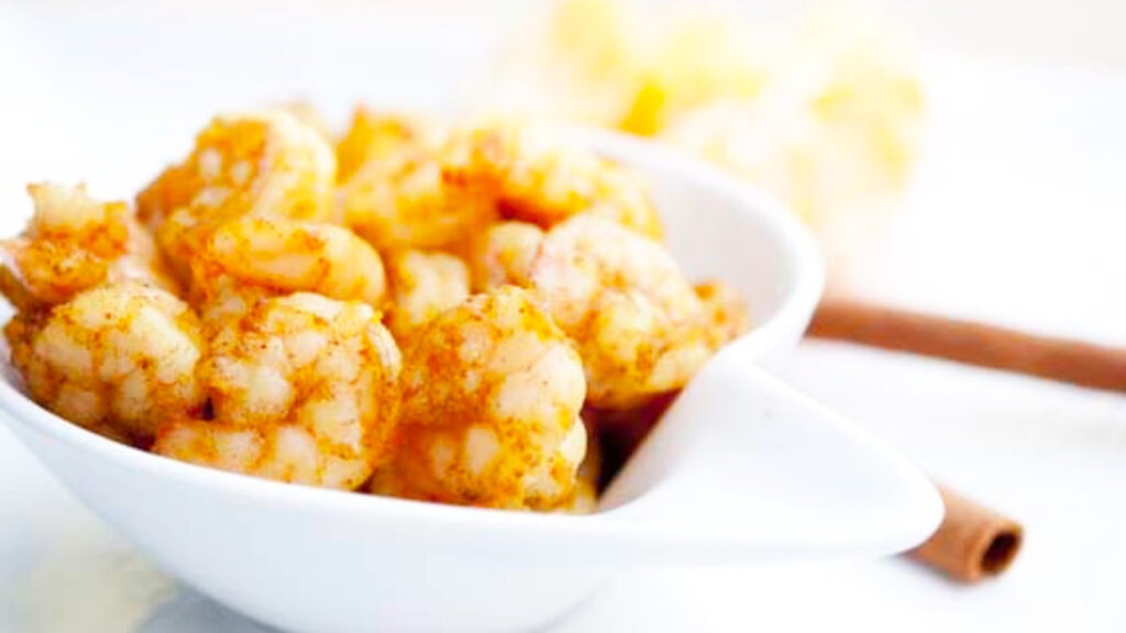 A white bowl holding spice orange cinnamon shrimp.