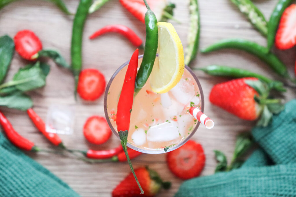Overhead view looking down on a Spicy Strawberry Zing Mocktail garnished with peppers and a lemon slice.
