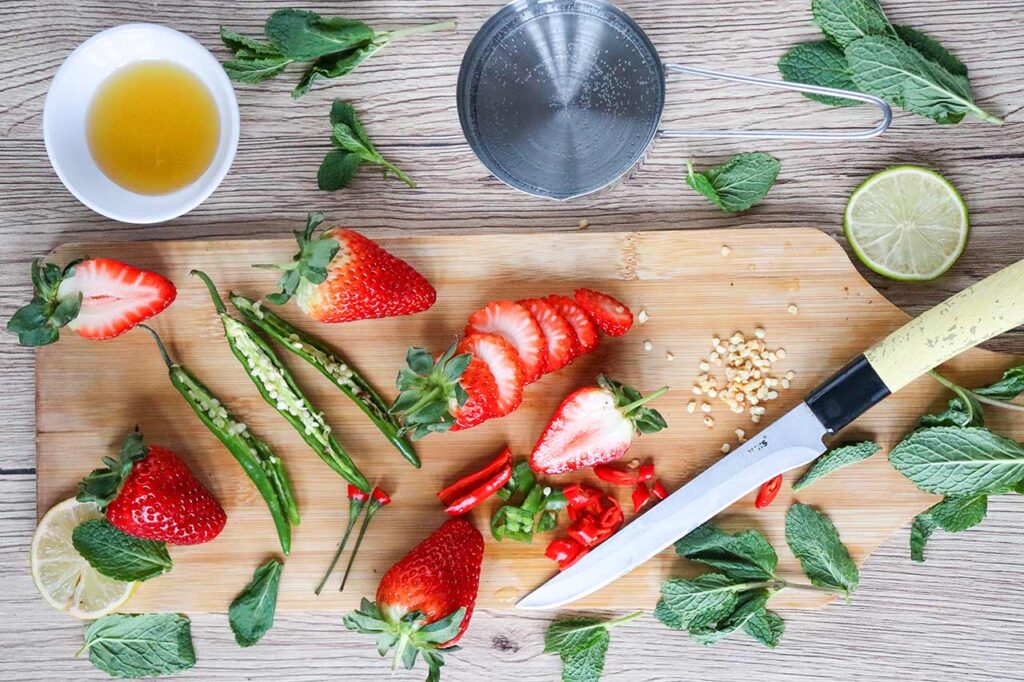 Cut strawberries and chili peppers on a cutting board.