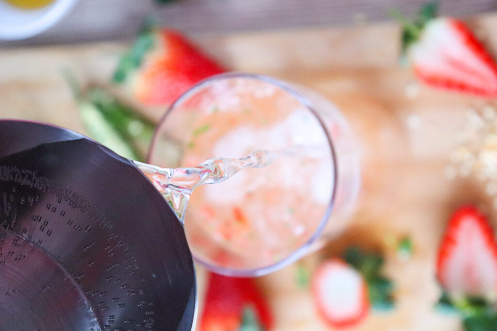 Pouring sparkling water into a glass with fruit blend.