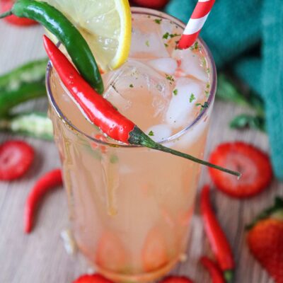 A semi-overhead view of a glass of strawberry mocktail garnished with peppers and a lime slice.