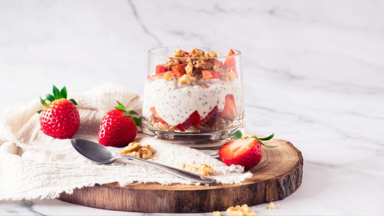 A single clear glass filled with strawberry chia pudding sitting on a cutting board with fresh berries.