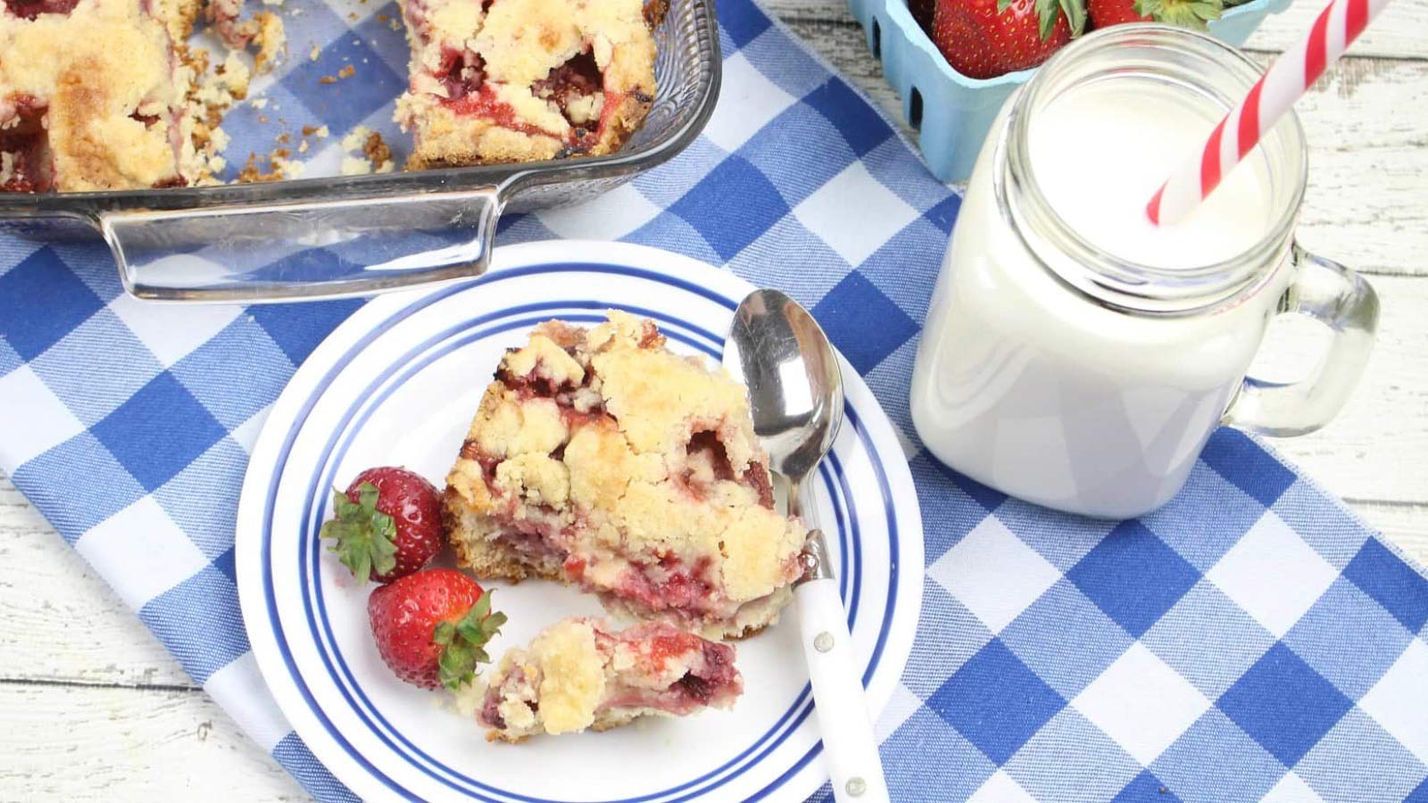 An overhead view of a white plate with a serving of strawberry cobbler on it. A glass of milk stands to the right.
