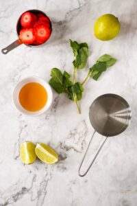Strawberry Mojito Mocktail ingredients on a white marble surface.