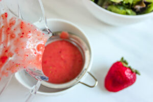 Pouring strawberry vinaigrette through a strainer.