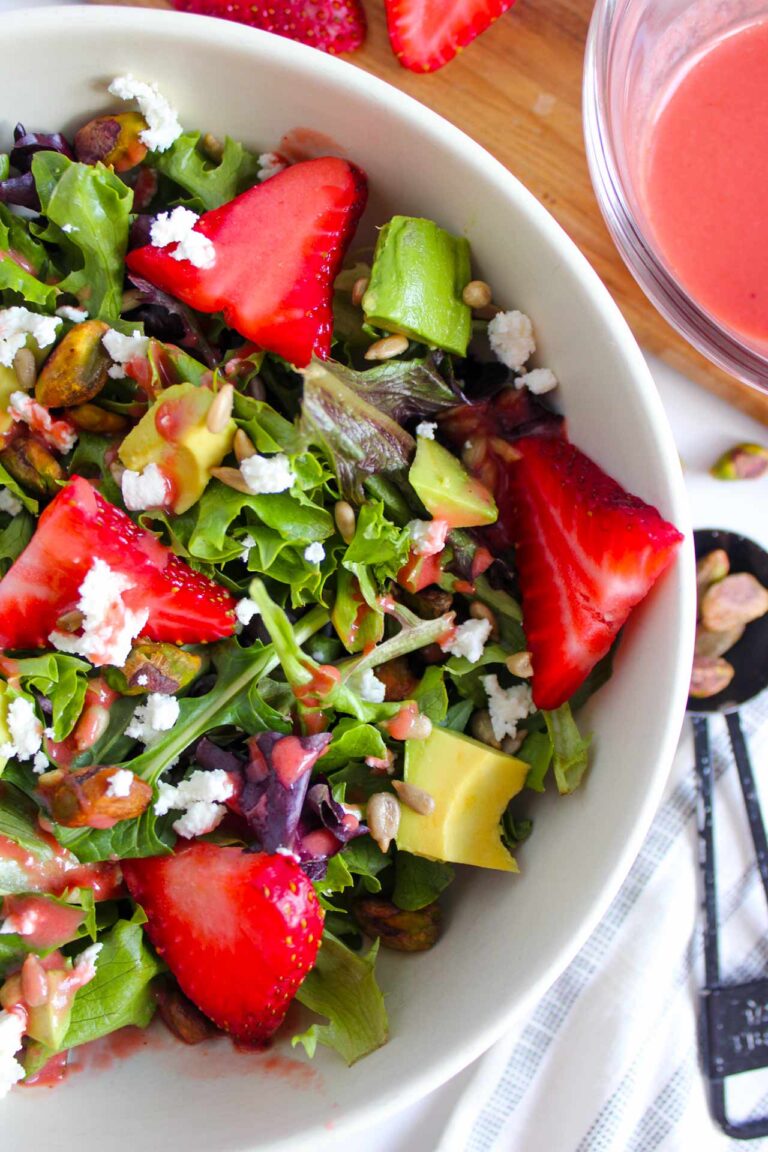 A partial view from overhead of a white bowl filled with Strawberry Pistachio Goat Cheese Salad.