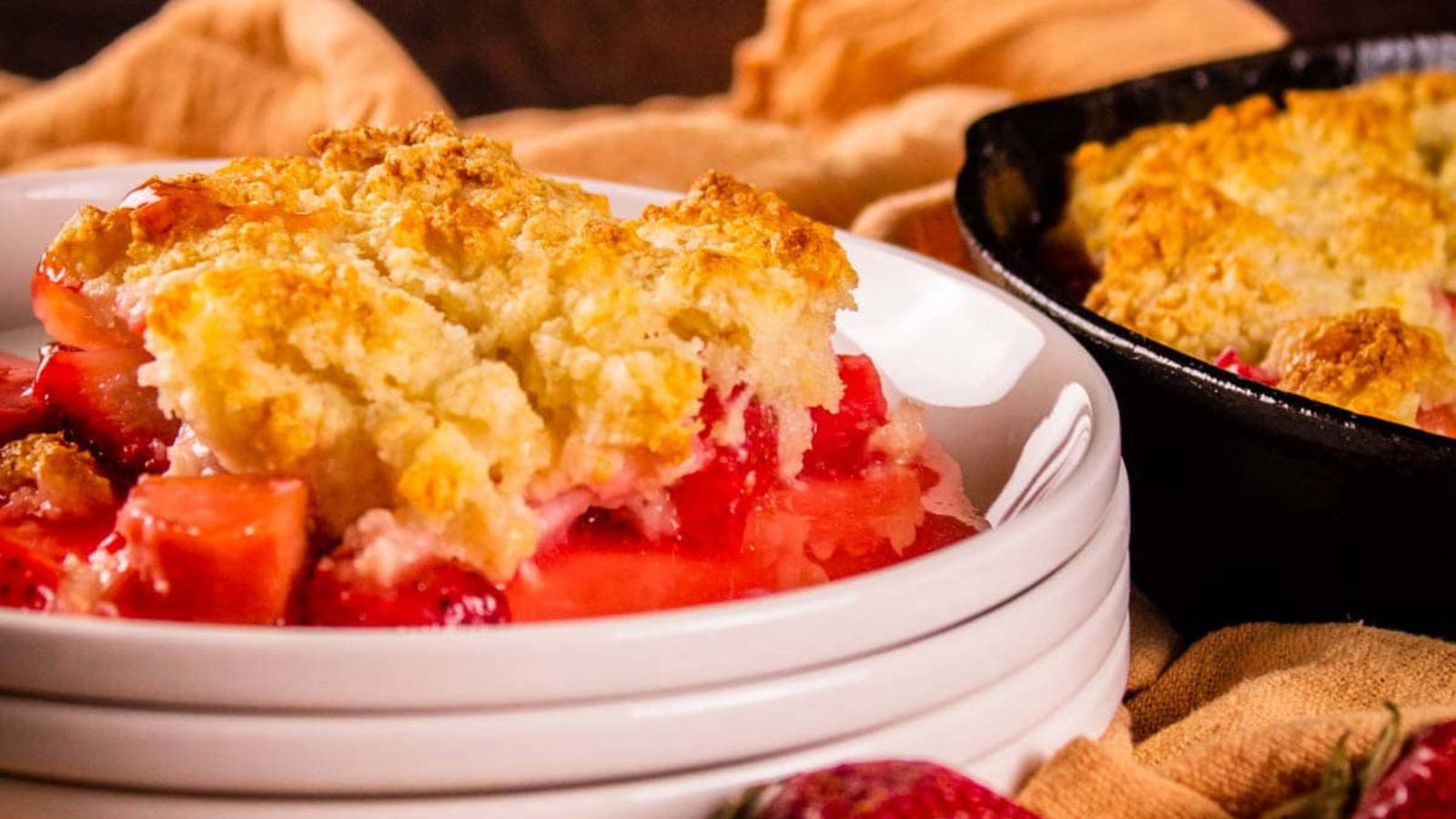 A closeup of a serving of strawberry rhubarb cobbler on a white plate.