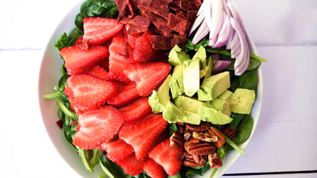 An overhead view of a strawberry spinach salad in a white bowl.