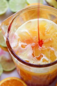 Pouring grenadine into a glass of juice with ice.