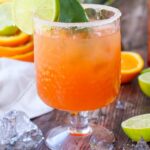A side view of a glass of Tequila Sunrise Mocktail garnished with a lime slice.