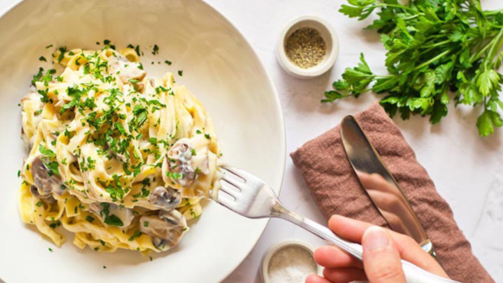 A hand holds a fork and reaches for a fork full of Vegan Fettuccine Alfredo
