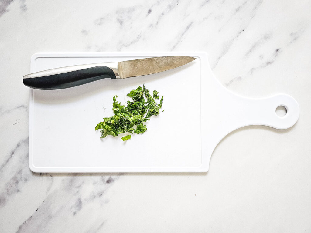 Chopped mint on a white cutting board with a knife.