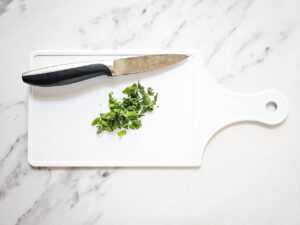 Chopped mint on a white cutting board with a knife.