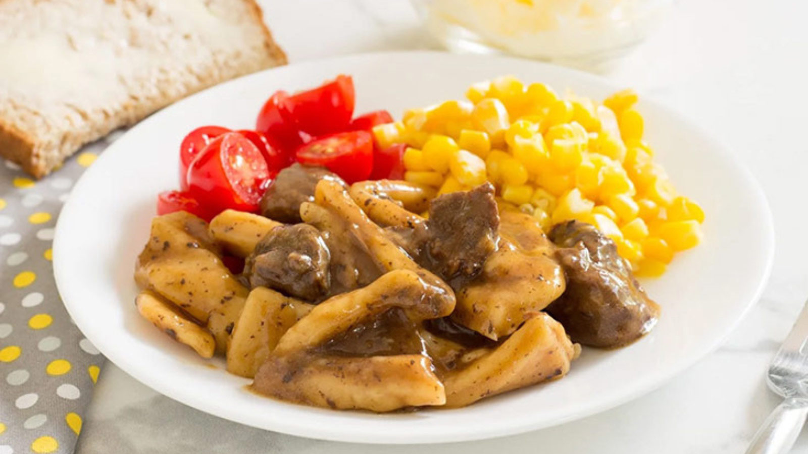 A white plate with beef noodles, corn and halved grape tomatoes.