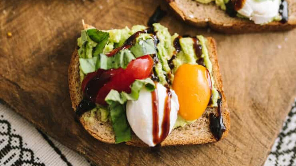 An overhead view of a half slice of caprese avocado toast on a cutting board.